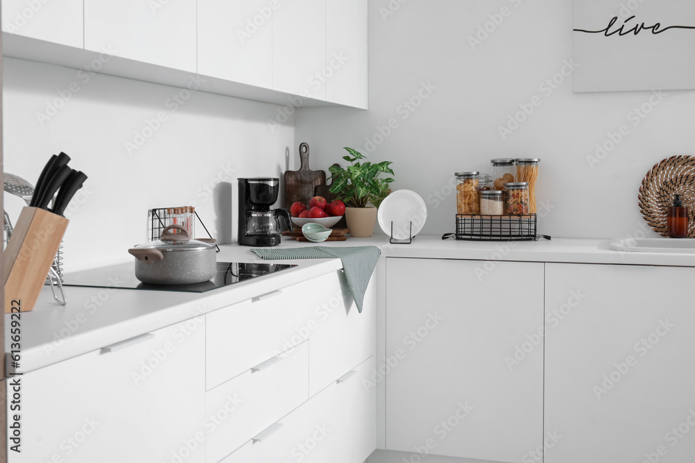 White kitchen counters with electric stove, cooking pot, coffee maker and plate rack