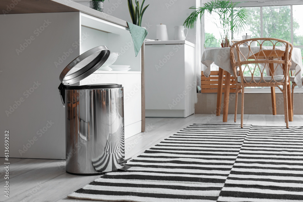 Opened metallic trash bin near table in interior of modern kitchen