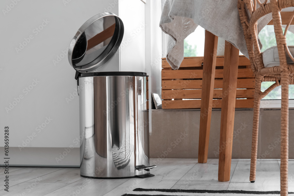 Opened metallic trash bin near table in interior of modern kitchen