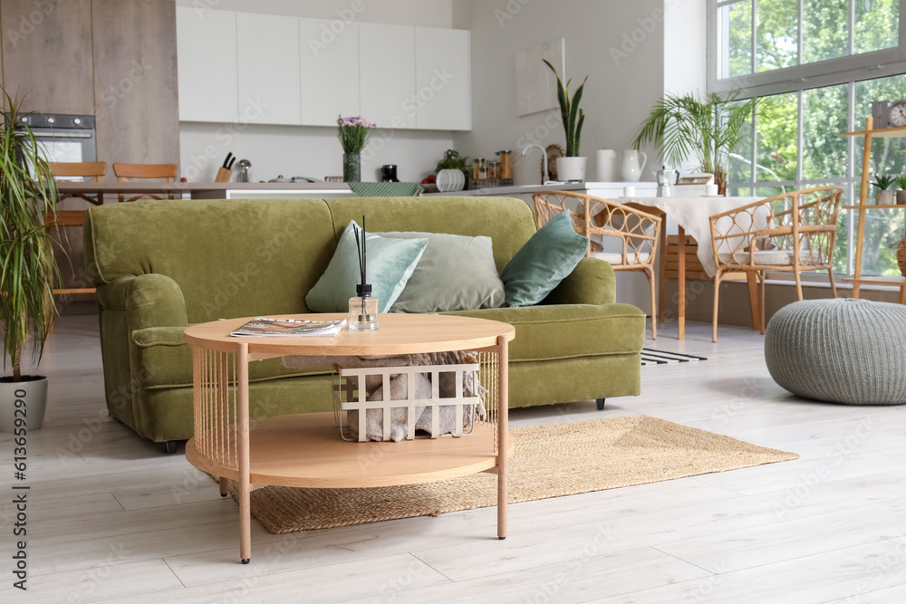 Interior of light open plan kitchen with green sofa and coffee table