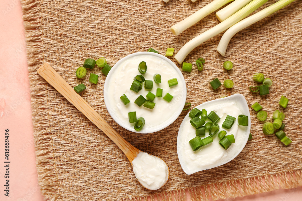 Bowl and gravy boat of tasty sour cream with sliced green onion on pink background