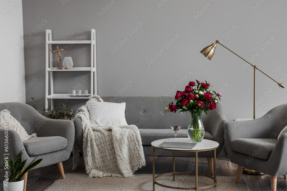 Vase with red peonies, glass and laptop on coffee table in living room