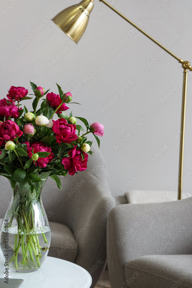 Vase with red peonies, glass and laptop on coffee table in living room