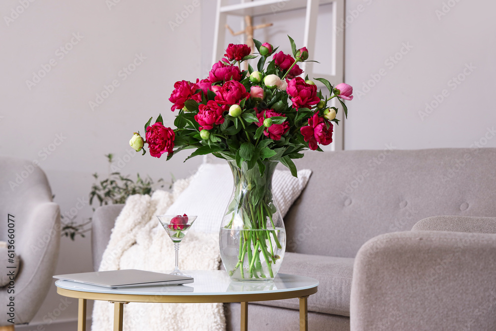 Vase with red peonies, glass and laptop on coffee table in living room