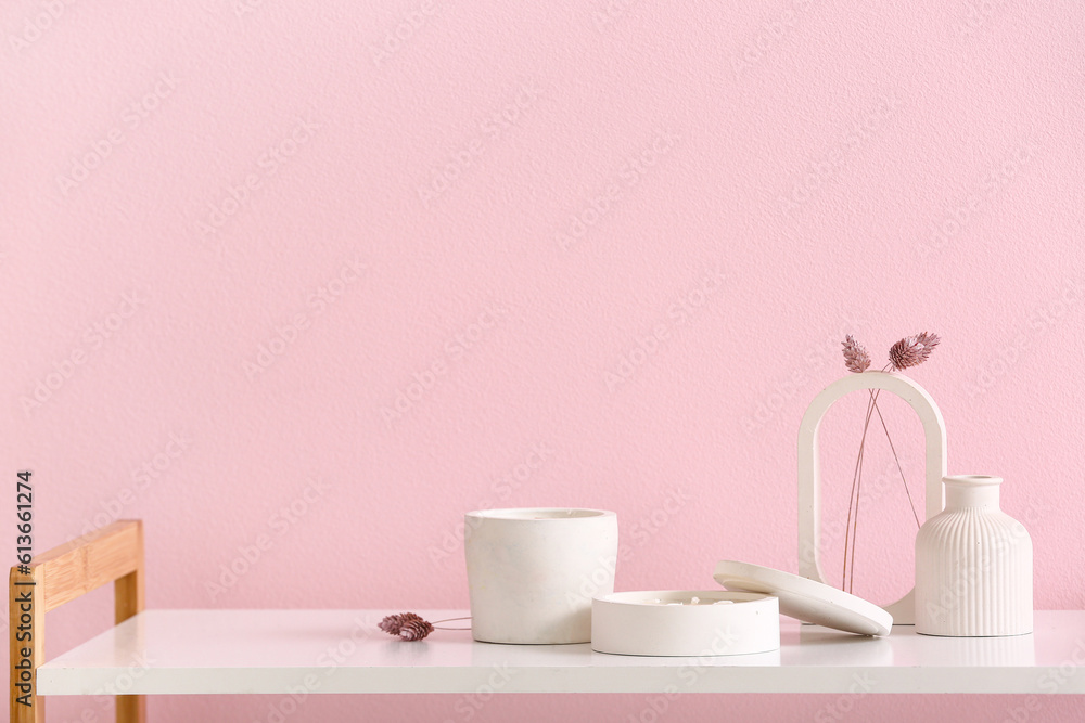 Holders with candles and decor on table near pink wall in room