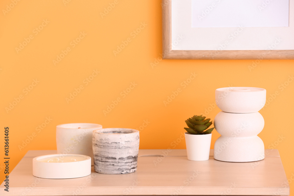 Holders with candles and houseplant near orange wall in room