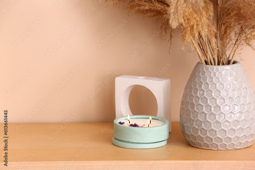 Holder with burning candle and pampas grass on table near beige wall in room