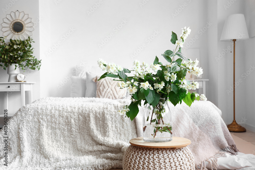 Vase with blooming jasmine flowers on pouf in interior of light bedroom