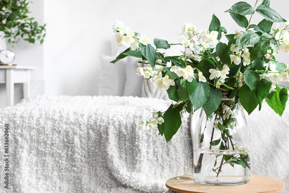 Vase with blooming jasmine flowers on table in interior of light bedroom