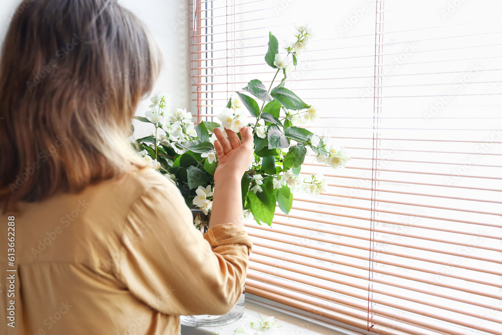 Woman enjoying blooming jasmine flowers in vase on windowsill