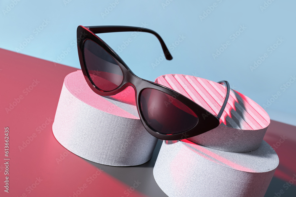 Podiums with stylish sunglasses on colorful background