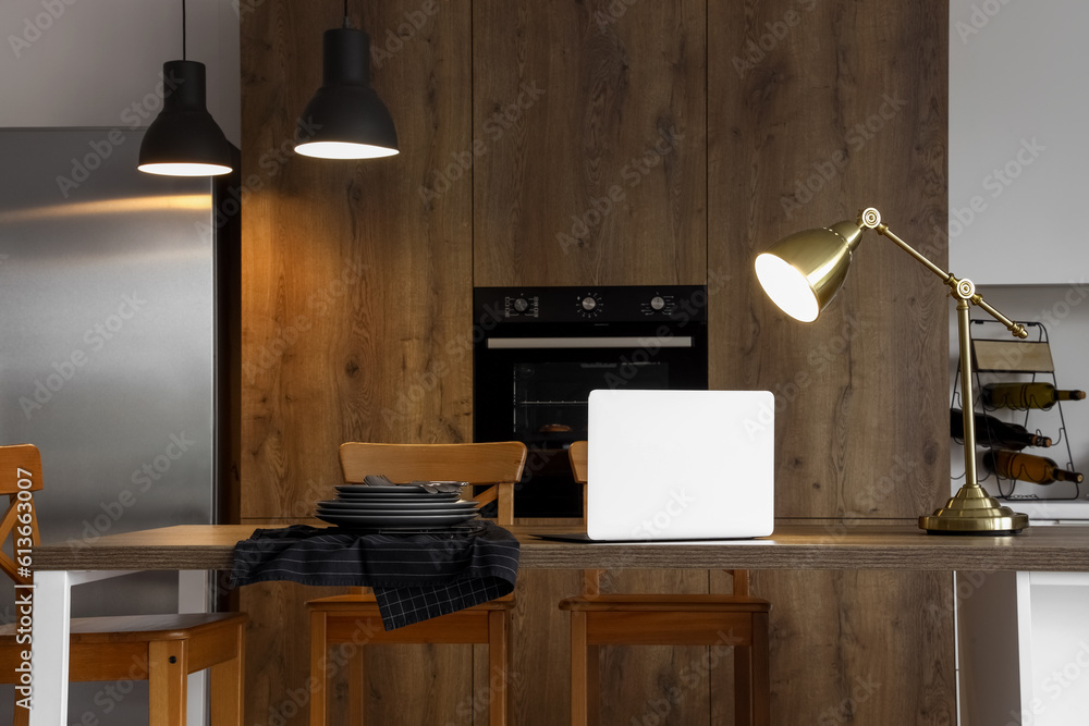 Interior of modern kitchen with glowing lamps and laptop on island table