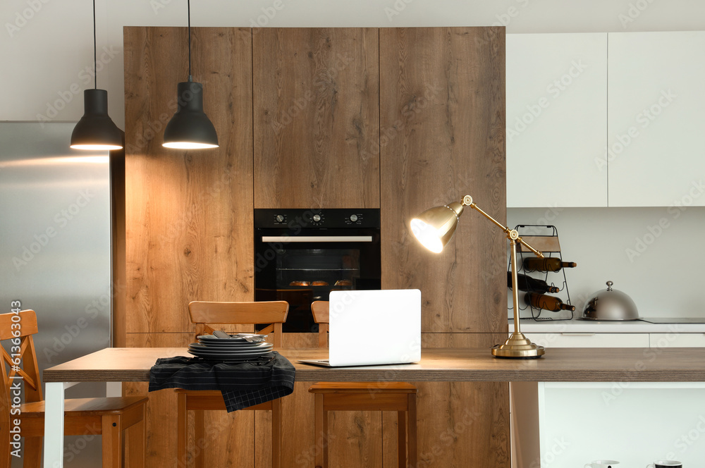 Interior of modern kitchen with glowing lamps and laptop on island table