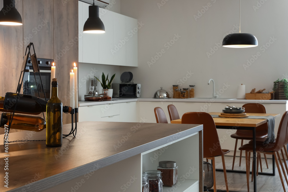 Interior of modern kitchen with dining table, island and glowing lamps