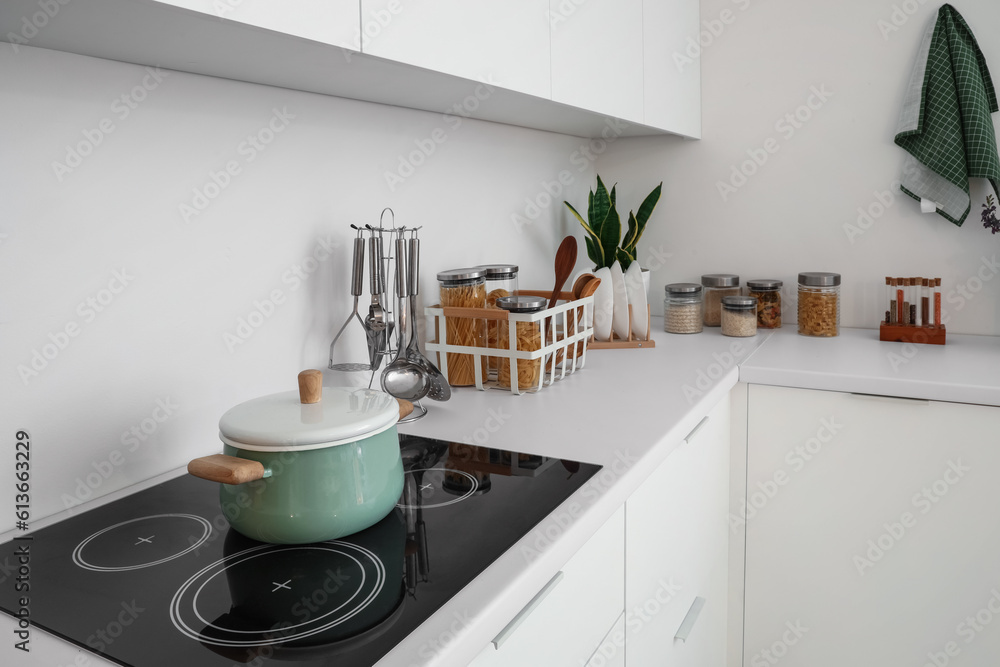 White counters with electric stove, cooking pot and utensils in interior of modern kitchen