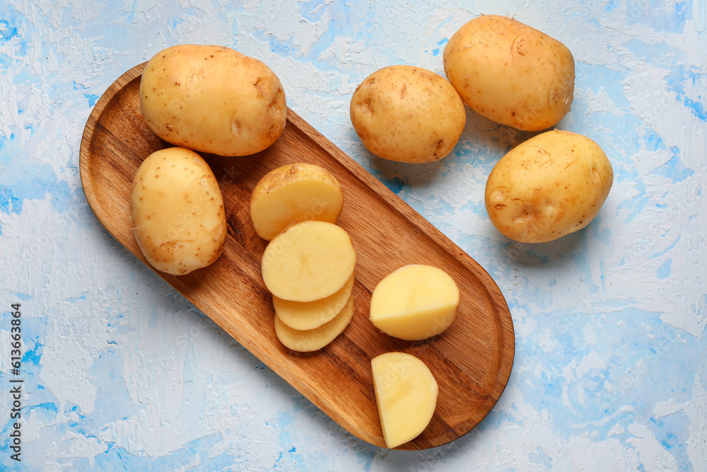 Wooden board with slices of raw baby potatoes on blue background