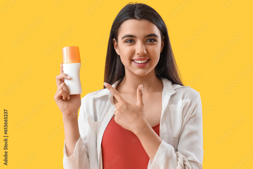 Young woman pointing at sunscreen cream on yellow background