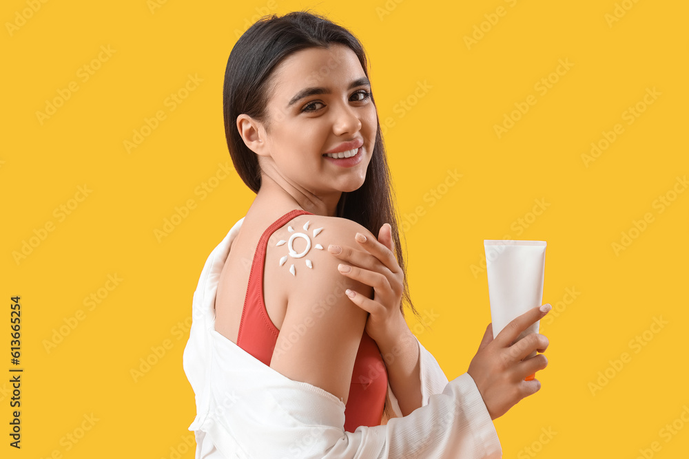 Young woman with sun made of sunscreen cream on her shoulder against yellow background