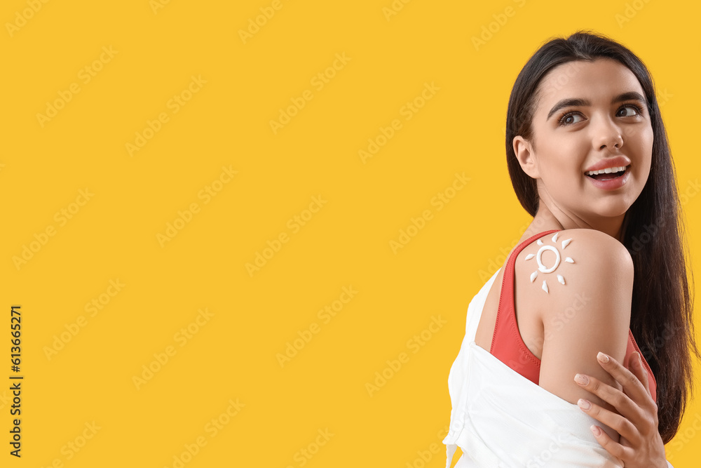 Young woman with sun made of sunscreen cream on her shoulder against yellow background