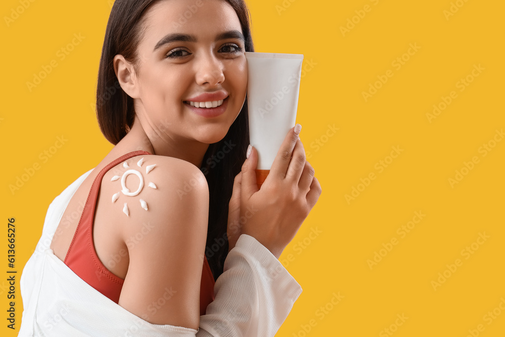 Young woman with sun made of sunscreen cream on her shoulder against yellow background, closeup