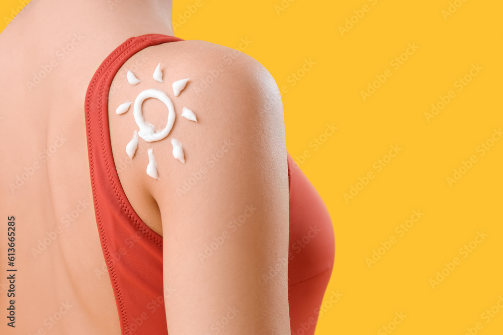 Young woman with sun made of sunscreen cream on her shoulder against yellow background, closeup