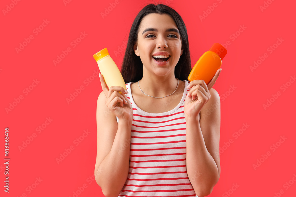 Young woman with bottles of sunscreen cream on red background