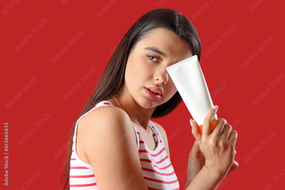 Young woman with sunscreen cream on red background, closeup