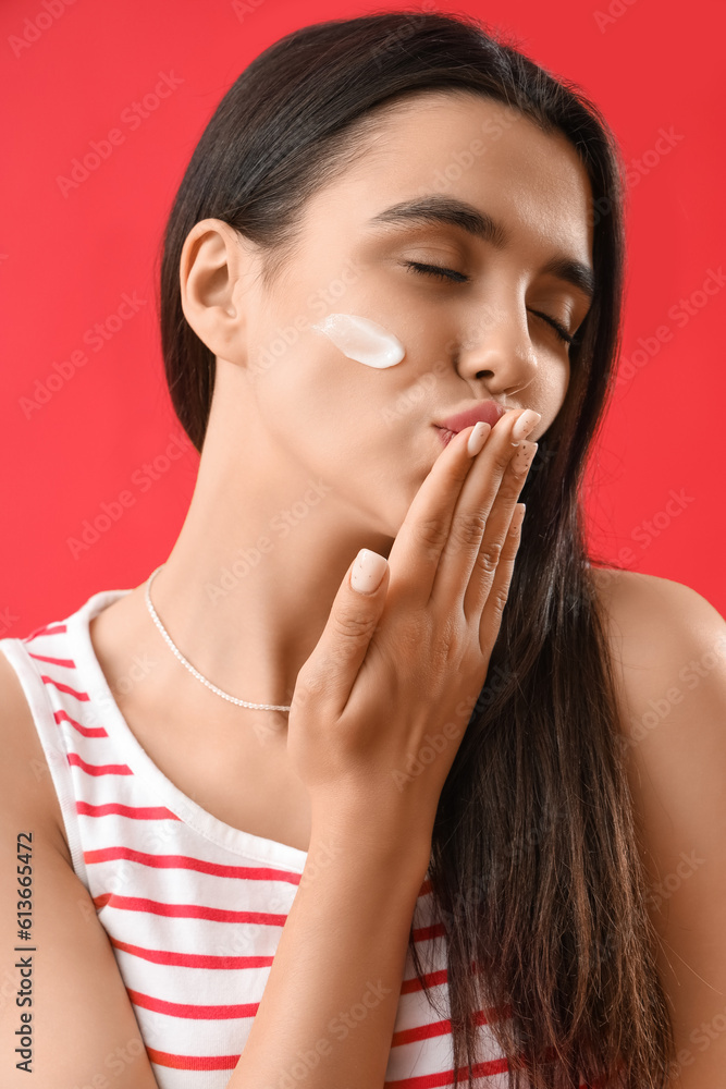 Young woman with sunscreen cream on her face blowing kiss against red background, closeup