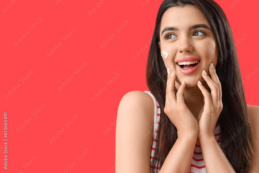 Young woman with sunscreen cream on her face against red background, closeup