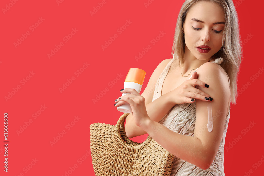 Young woman applying sunscreen cream on red background