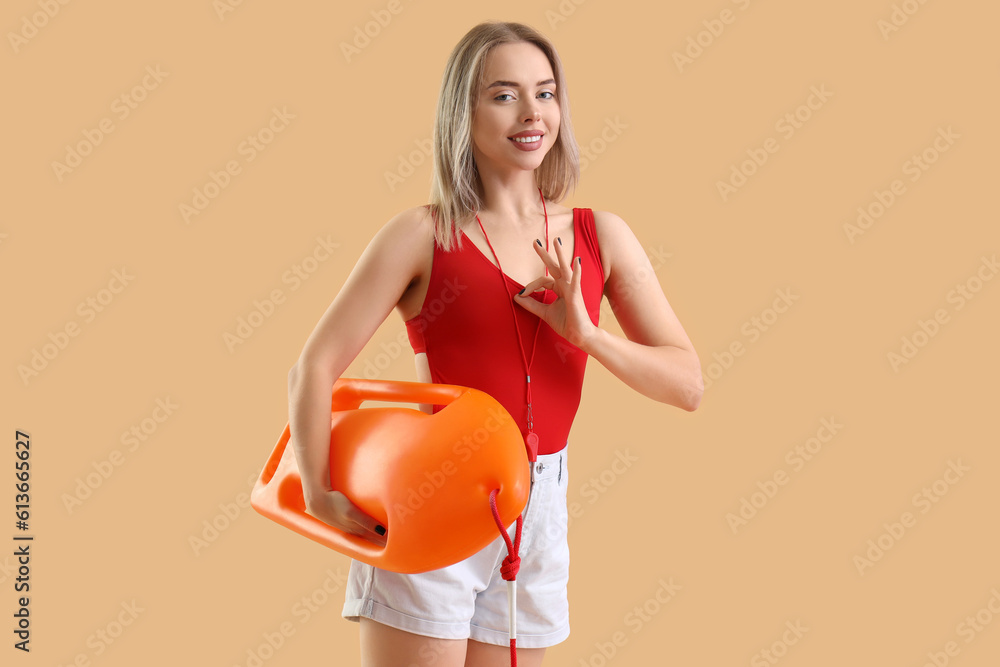 Female lifeguard with rescue buoy showing OK on beige background