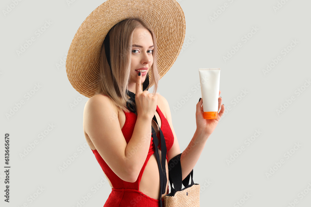 Thoughtful young woman with sunscreen cream on light background