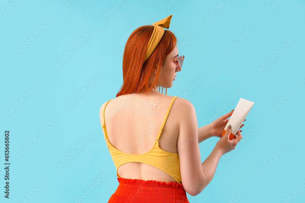 Young woman with sun made of sunscreen cream on blue background, back view