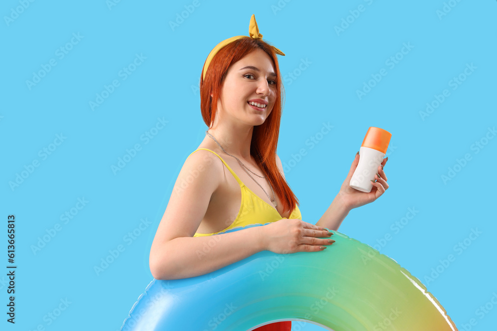 Young woman with sunscreen cream and inflatable ring on blue background