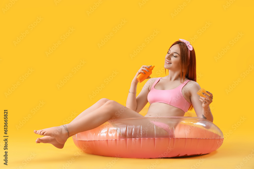 Young woman with sunscreen cream and inflatable ring on yellow background