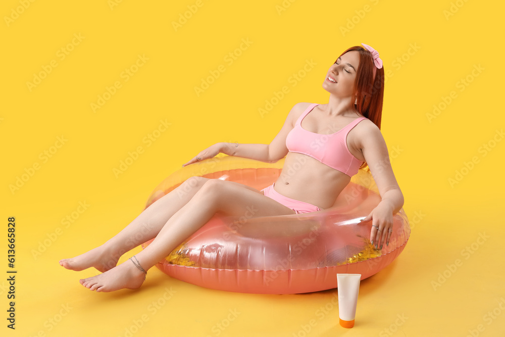 Young woman with sunscreen cream and inflatable ring on yellow background