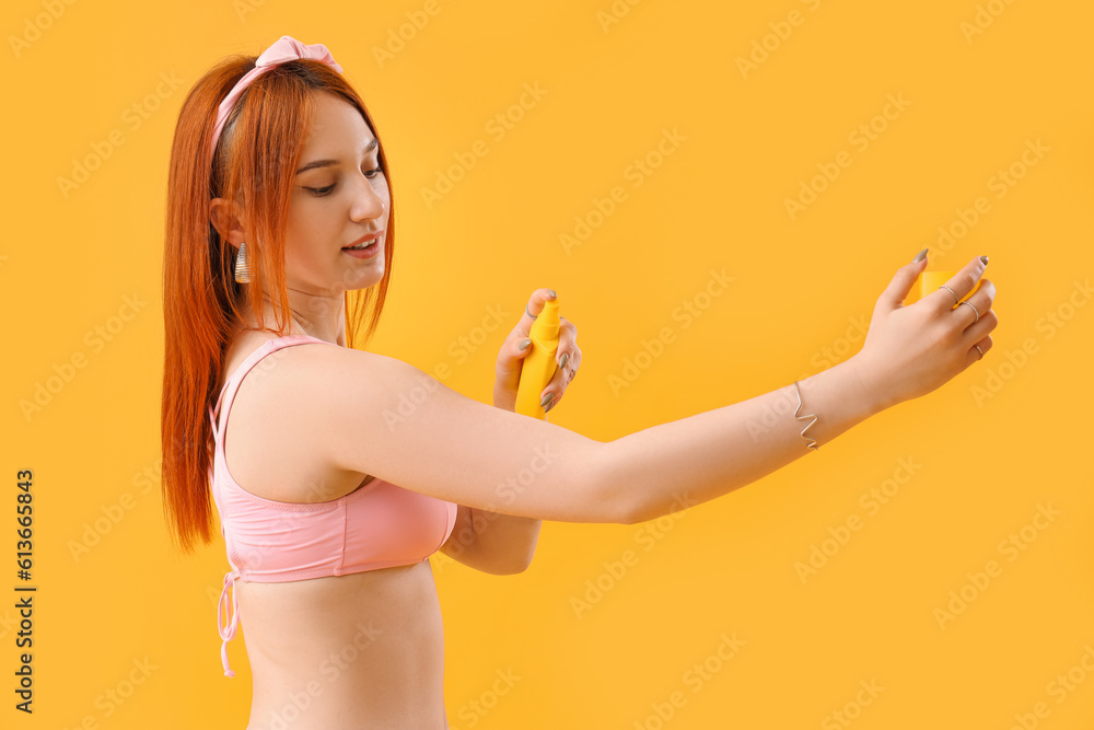 Young woman applying sunscreen cream on yellow background