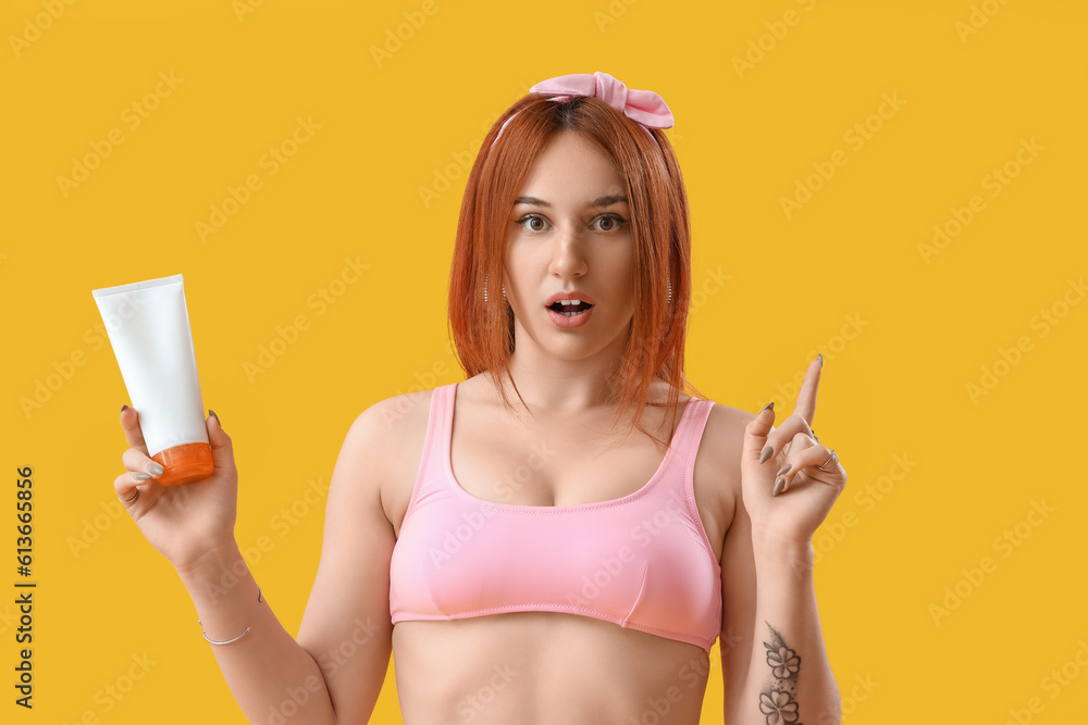 Young woman with sunscreen cream pointing at something on yellow background