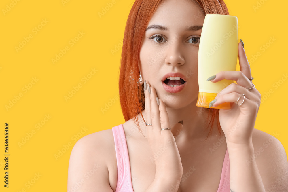 Surprised young woman with sunscreen cream on yellow background, closeup