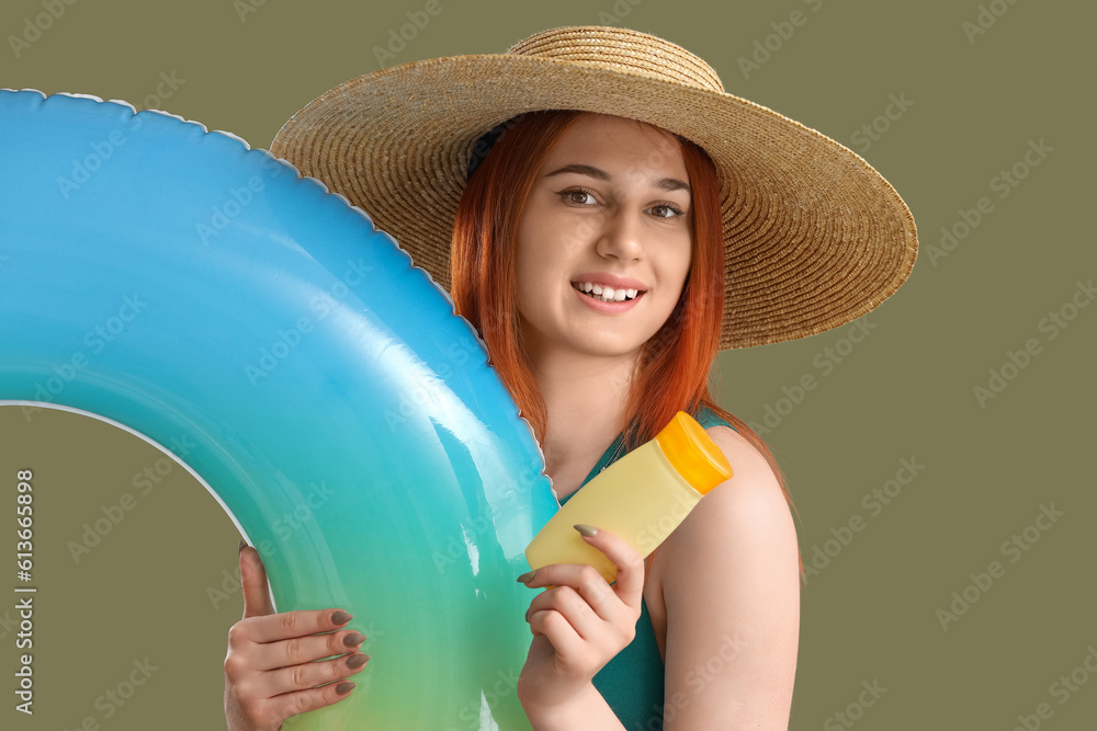 Young woman with sunscreen cream and inflatable ring on green background