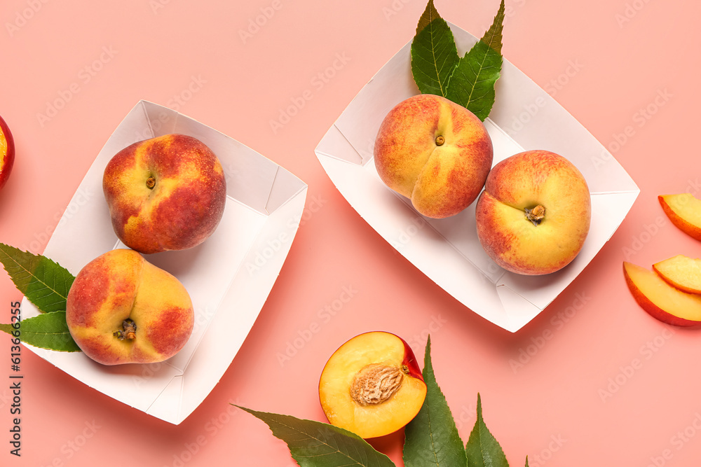 Paper plates with sweet peaches and leaves on pink background