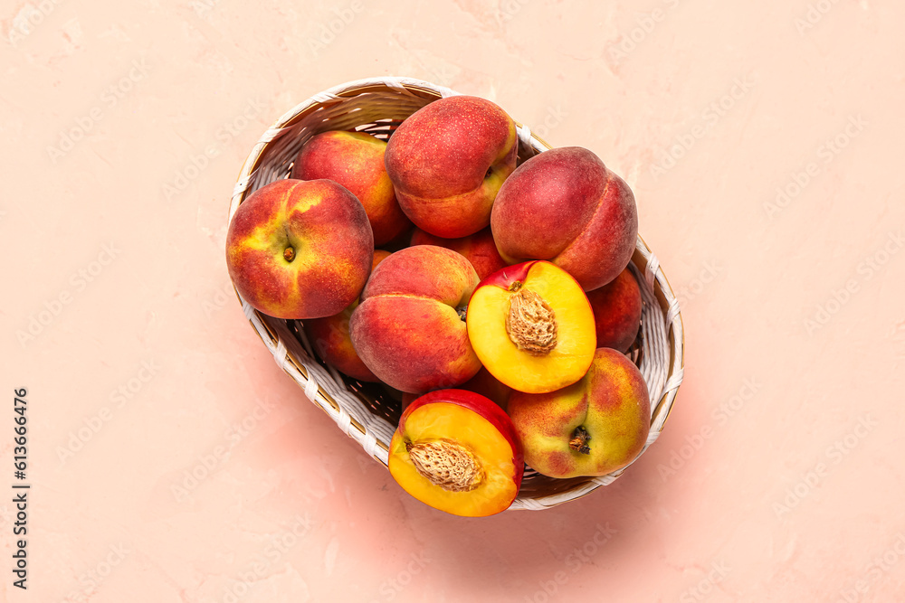 Wicker bowl with sweet peaches on pink background