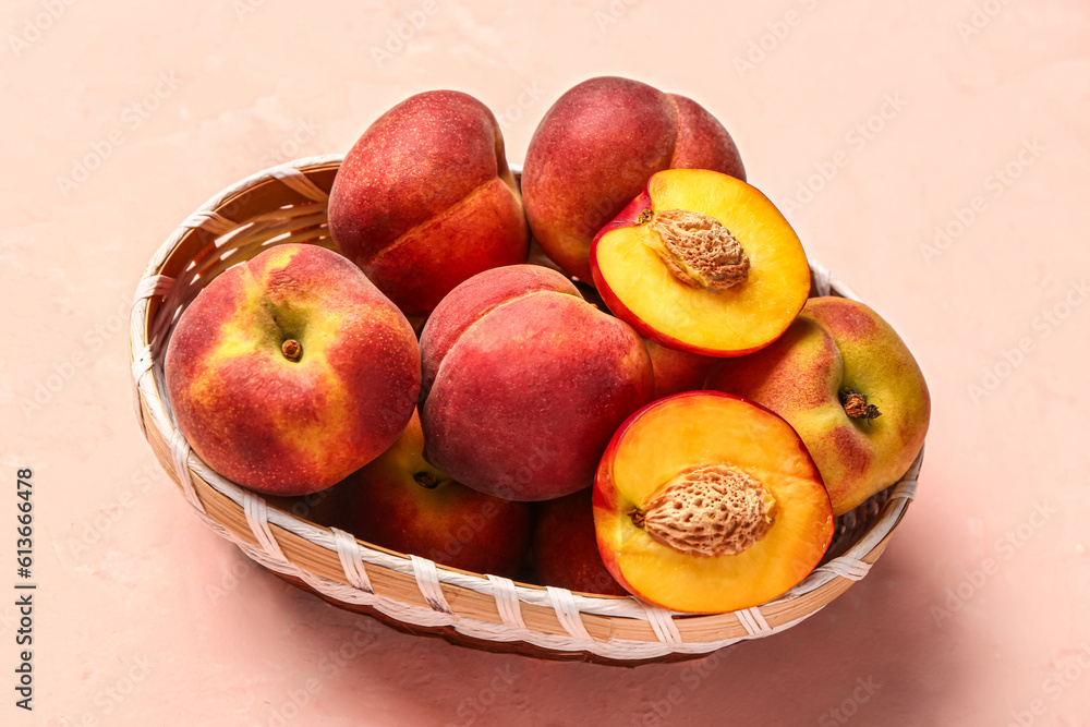 Wicker bowl with sweet peaches on pink background