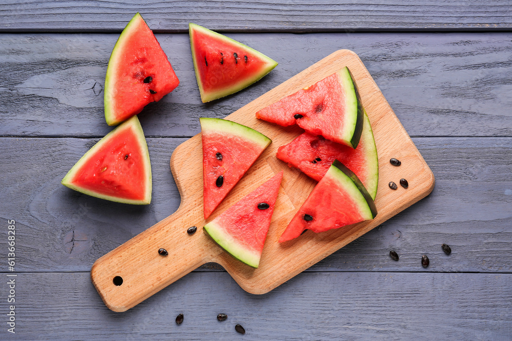 Board with pieces of fresh watermelon and seeds on blue wooden background