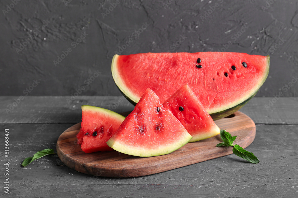 Board with pieces of fresh watermelon and mint on black wooden table