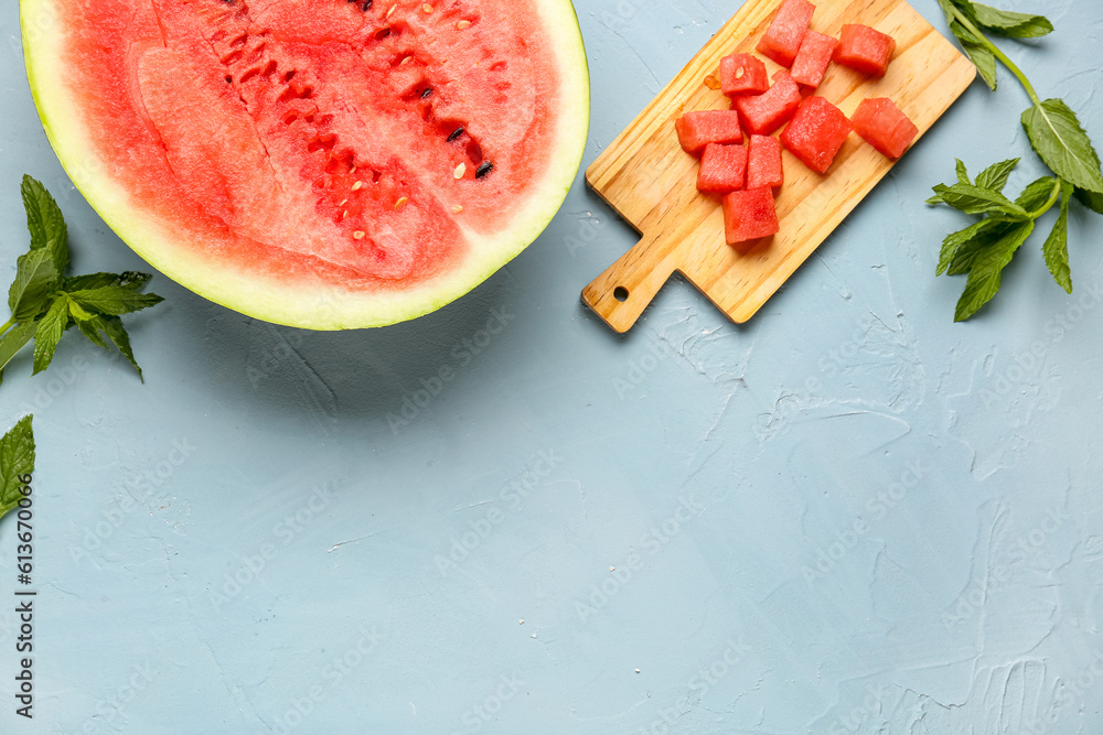 Half of fresh watermelon and board with pieces on blue background