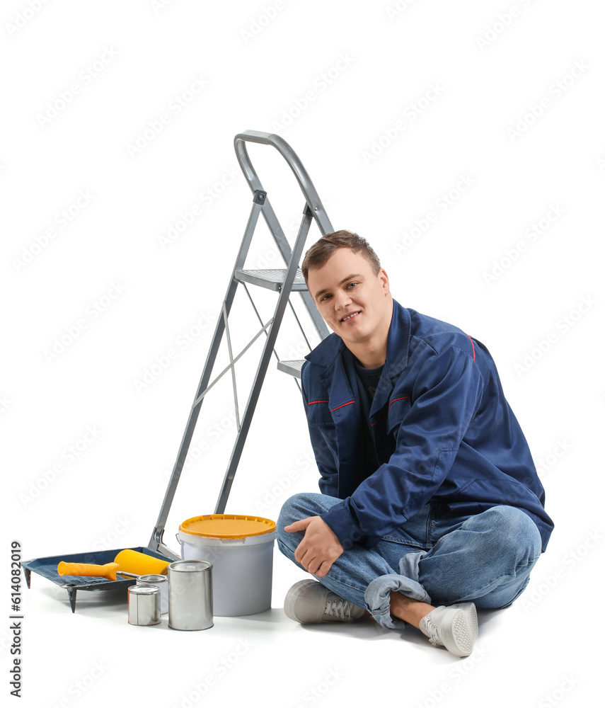 Young man with ladder and cans of paint sitting on white background