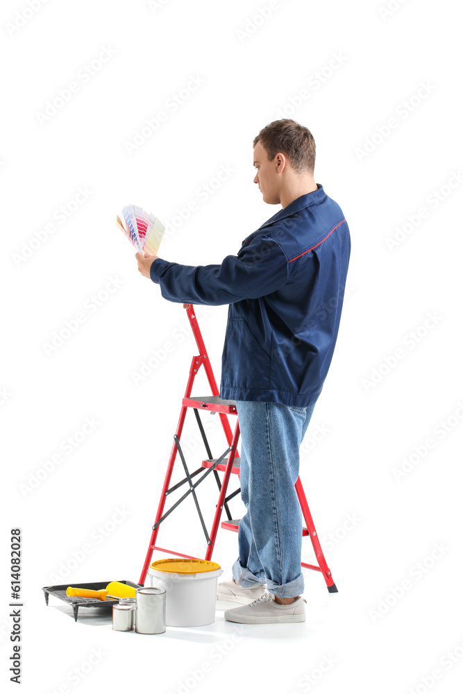 Young man with palettes, ladder and cans of paint on white background