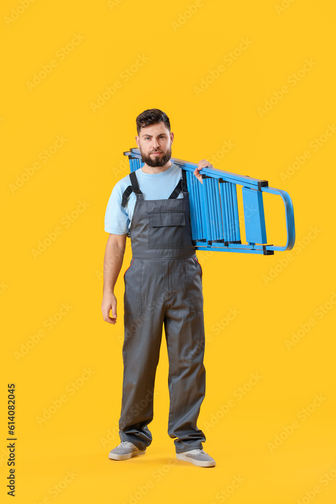 Male worker with ladder on yellow background