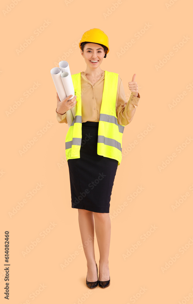 Female architect in vest and with drawings showing thumb-up on beige background